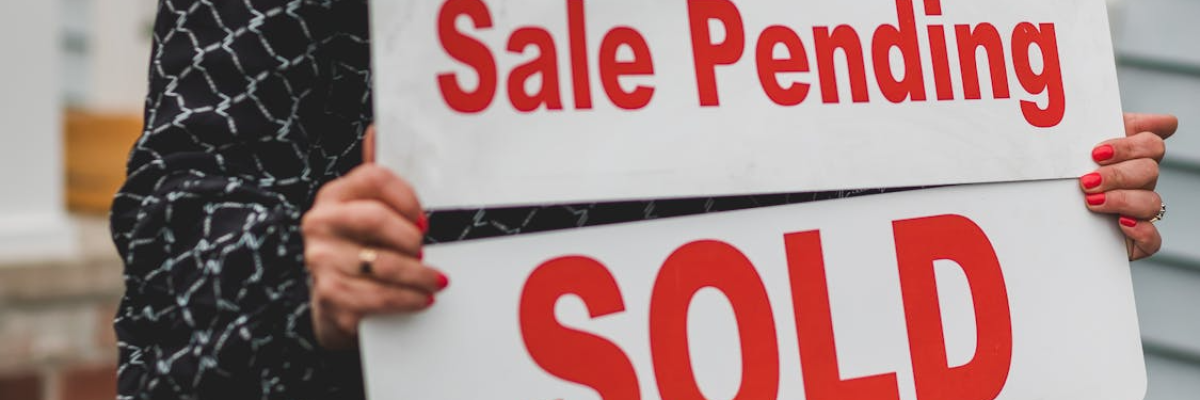 A person holding a sale pending and sold sign