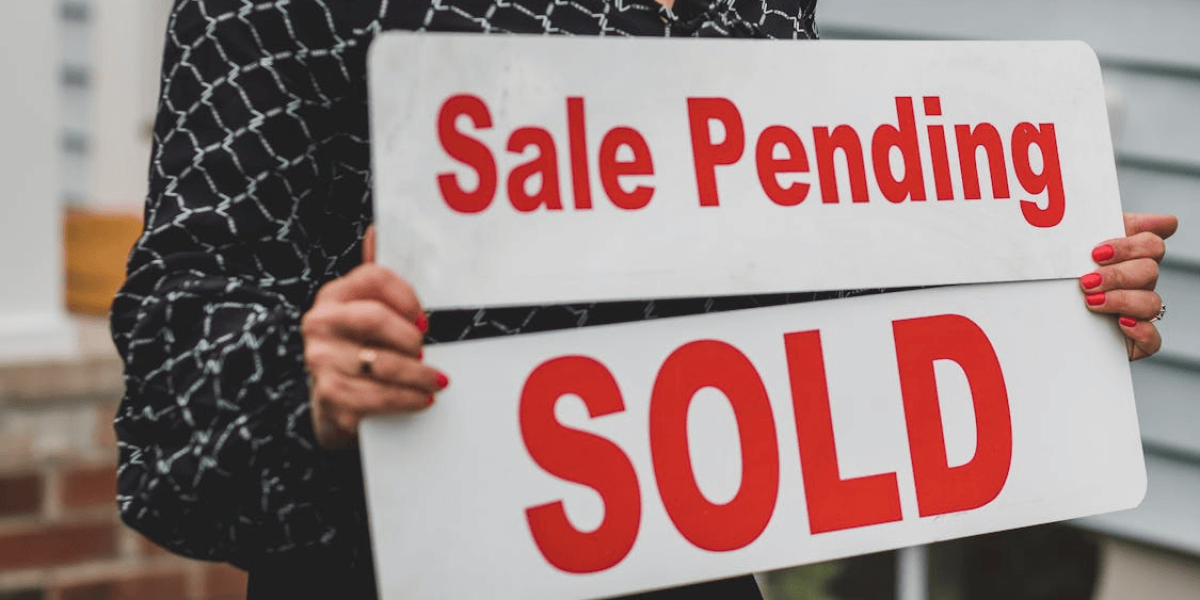 A person holding a sale pending and sold sign